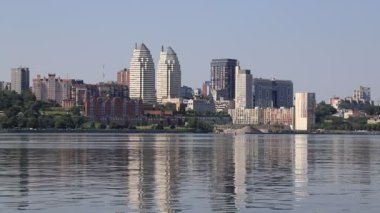 Nehir kıyısındaki büyük şehir. Ukrayna şehri Dnipro, Ukrayna. Güzel modern kuleler, binalar, gökdelenler yaz sabahının erken saatlerinde suya yansıyor..