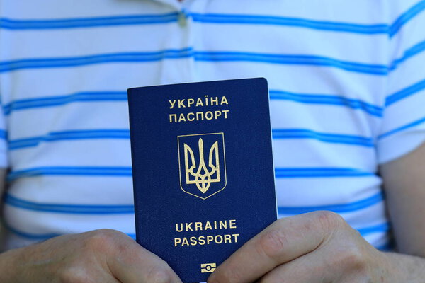 Мужчина держит в руках украинский паспорт с надписью на украинском языке - паспорт Украины. Концепция путешествий, беженец, турист, эмигрант, мобилизация, мигрант.