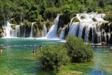 Turistler yazın şelalenin yanındaki gölde yüzerler. Büyük, güzel Hırvat şelaleleri, dağlar ve doğa. Krka Ulusal Parkı, Hırvatistan 1806 2019