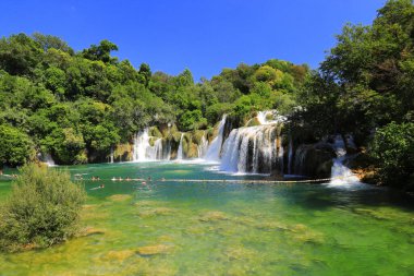 Turistler yazın şelalenin yanındaki gölde yüzerler. Büyük, güzel Hırvat şelaleleri, dağlar ve doğa. Krka Ulusal Parkı, Hırvatistan 1806 2019