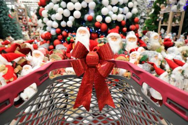 Trolley for goods and products in Christmas supermarket against background of New Year tree and toy Santa Claus. Shopping, sale. Shopping cart in wholesale store before Christmas clipart