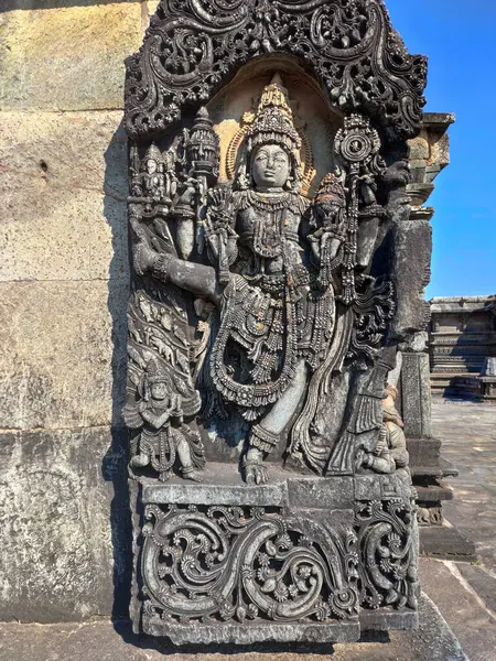 Vishnu 'nun detaylı bir taş oyması Chennakeshava Tapınağı' nda bir duvarı süslüyor. Vishnu dinamik bir şekilde ayakta duruyor, sağ bacağını kaldırıyor, giysi, mücevher ve fizikte karmaşık detaylar sergiliyor..