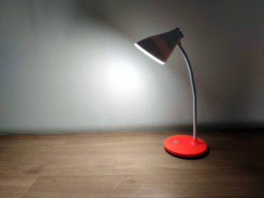 Beyaz kıvrımlı boyunlu modern bir kırmızı masa lambası, şarj edilebilir pillerle çalışan, yumuşak LED ışığı ahşap bir yüzeye yayar, minimalist, rahat bir atmosfer yaratır..