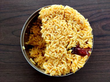 Paslanmaz çelikten tiffin içinde soğan pilavı yakın plan, kırmızı biberli canlı sarı. Yumuşak, iyi pişmiş tahıllar bu lezzetli Hint yemeğinin altını çiziyor..