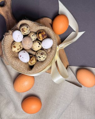 Ahşap bir yüzeyde keten peçete ve saten kurdelenin arasına yerleştirilmiş pastel Paskalya yumurtalarının bir çeşidi şenlikli ve zarif bir bahar ortamı yaratıyor..