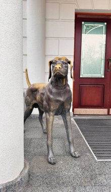 Sütunları olan bir evin yanında duran bir köpek heykeli, bir kır evinin dekorasyonu. Kırmızı ahşap kapılı, vitraylı..