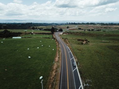 Dağlardan, rotorua 'dan, Yeni Zelanda' dan uzak bulutlu bir günde, büyük yeşil otlak ovasını trafiğin geçmediği uzun bir yol.