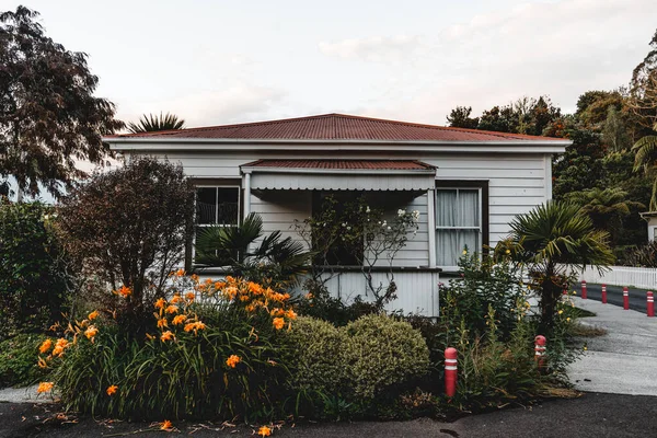 曇り空 西地区 ニュージーランドの下で穏やかな静かな村のオレンジの花や緑の植物に囲まれた狭い通りに美しい木造の家 都市の概念 — ストック写真
