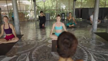 Kadın yoga eğitmeninin sınıfa önderlik etmesi ve öğrencileriyle konuşması. Öğrenciler dikkat ediyor - 4K Yatay video