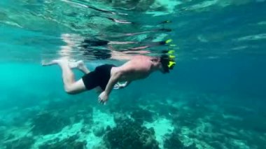 Mercanların arasında yüzen maskeli çocuk kameraya bakar ve her şeyin yolunda olduğunu gösterir.