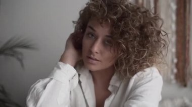 Genç bir kadın saçlarına dokunuyor ve oturma odasında gülümsüyor - 4K Yatay Video