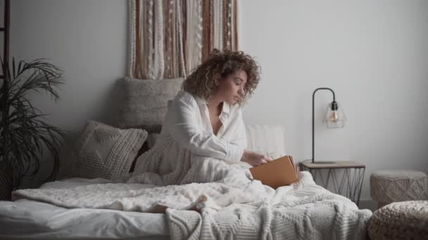 彼女の部屋でベッドの上で本を読んでいるリラックスした美しい女性 4K水平ビデオ — ストック動画