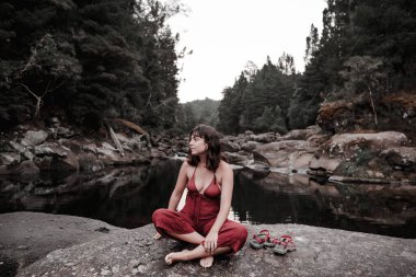 Yalınayak genç kadın sandaletleri bir yana kayanın üzerinde oturuyor - yaşam tarzı kavramı