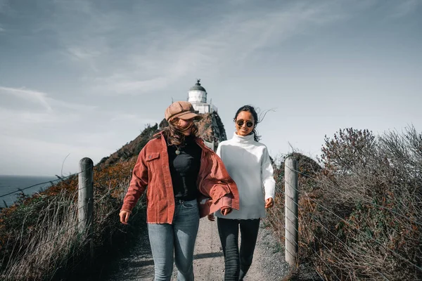 stock image two happy caucasian girls having fun running towards the camera up the narrow dirt path coming from the impressive lighthouse, nugget point, new zealand - Travel concept