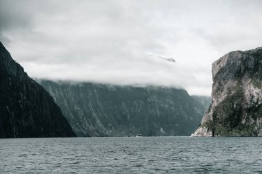 Turistlerle dolu tekneler, gri bulutlarla dolu bir gökyüzü, Milford sesi ve Yeni Zelanda 'nın altında etkileyici kayalık fiyortlar arasında büyük gölün sularında yüzüyor.