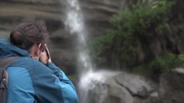 Adam sırtüstü yatmış Truman hipodromunda doğal şelalenin fotoğrafını çekiyor, Yeni Zelanda - seyahat yaşam tarzı konsepti