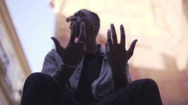 Adam sokakta otururken ellerini çırpıyor ve el hareketi yapıyor - yaşam tarzı konsepti