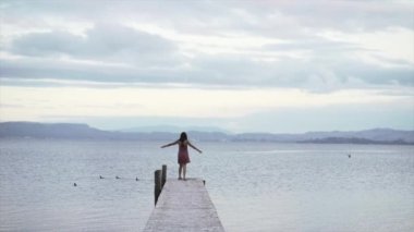 Tarawera Glampling, Yeni Zelanda 'da, deniz kenarında bir köprüde kollarını havaya kaldırmış bir kadın. - Seyahat konsepti