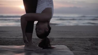 Yetişkin bir kadın plajda güneşin doğuşuyla hasırının üzerinde geriniyor.