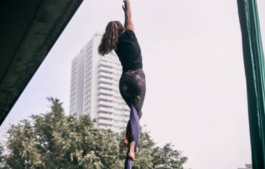 Beyaz kadın parktaki bir köprüde asılı halde havadan ipekler üzerinde pratik yapıyor. Doğayla iç içe..