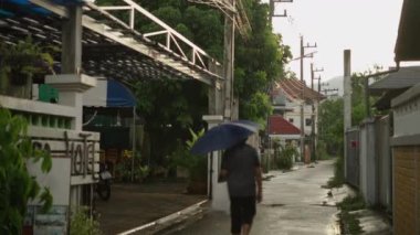 Chiang Mai 'de bir sokakta çanta ve şemsiyeyle yürüyen yaşlı bir adam.