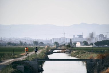 Nehir kenarındaki bisiklet yolunda bisiklet süren iki beyaz adam, Albufera Doğal Park Valencia, İspanya - Doğa Fotoğrafçılığı