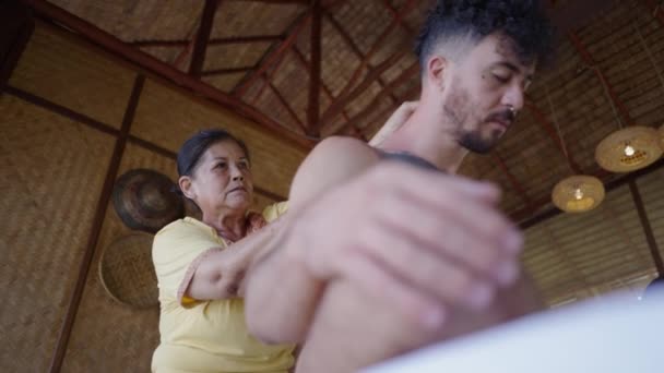 ネイティブ タイの女性はサロン スパで若い白人のコスチュマーに腰痛のための癒しのマッサージを提供します タイの伝統 — ストック動画
