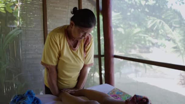 タイマッサージを与える高齢女性は 女性の足に圧力をかけ コスチュマーに話しかけます スローモーションショット タイの伝統 — ストック動画