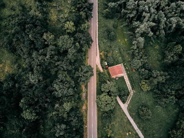 Drone view of the lonely straight narrow road near the house among the trees and greenery - Travel concept