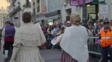 İki yetişkin kadın geçit töreninin ortasında yaşlı bir adamla konuşuyor. İspanyol gelenekleri.