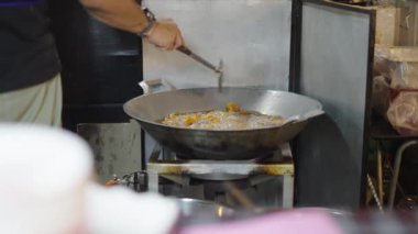 Tayland Bangkok Sokak Pazarı 'nda büyük bir tencerede büyük bir spatulayla Asyalı erkek tavuk kızartıyor.