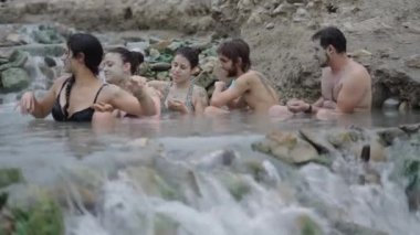 Arka arkaya beş kişi nehirde birbirine çamur atıyor. Doğal Spa konsepti.