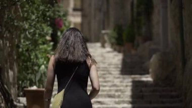 Genç Avrupalı bir kadın kırsal bir kasabada bitkilerle süslenmiş bir caddenin merdivenlerinden yukarı çıkıyor. - Paradisiac İspanyol mekanları