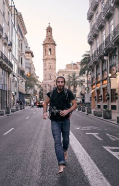 Sırtında büyük bir sırt çantası olan beyaz bir genç adam çıplak ayakla şehir caddesinde, Valencia 'da, İspanya' da sırt çantasıyla geziyor.