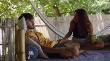 Güzel beyaz kadın tropikal sahilde oturuyor ve ufuk çizgisine gülümseyen 4K yatay videoya bakıyor.