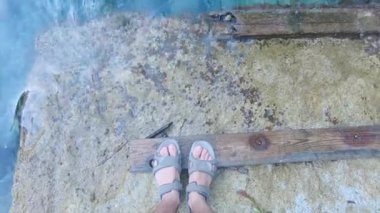 Tahta tahtalarla taştan bir sahilde sandalet giymiş ayakların durağan görüntüsü. - Paradisiac İspanyol mekanları