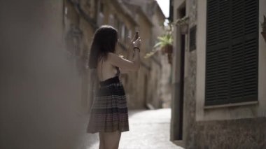 Genç bir kadın boş bir köy sokağında akıllı telefonuyla fotoğraf çekiyor. - Paradisiac İspanyol mekanları