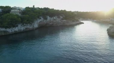 İspanya Adası turizminde kayalar ve çam ağaçlarıyla çevrili bir sahilde harika bir gün batımı.