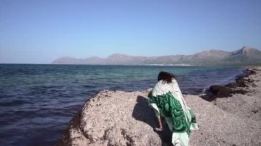 Uzun saçlı ve battaniyeli çocuk Sea Rock Adası turizmine tırmanıyor.