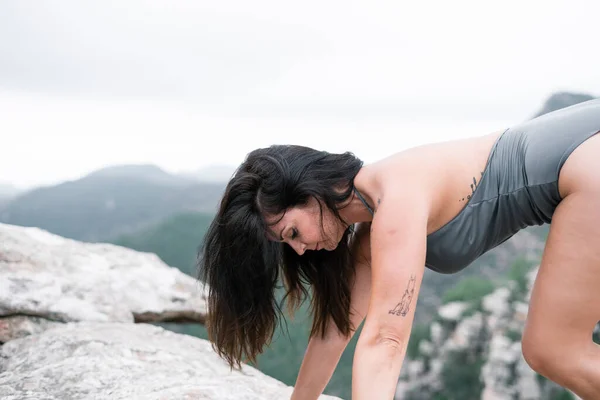 Caucasian mature woman with long brunette hair doing gymnastics exercises on the big rocks next to nature - Spiritual concept