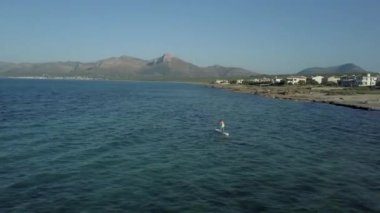 Yetişkin adam denizde sörf yapıyor. Bir köy adası turizminin yanında.