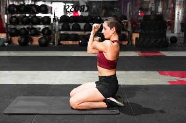 Kafkasyalı genç bir kadın spor salonunda ince bir hasırın üzerinde egzersiz yapıyor.