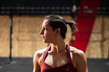 Geniş bir spor salonunda saçında at kuyruğu olan, beyaz tenli, esmer bir kadın.