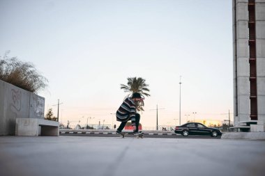Açık bir günde, gün batımında şehirde kaykay üzerinde çömelmiş çizgili spor ayakkabılı beyaz çocuk - yaşam tarzı konsepti