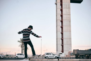 Gürültülü şehirde fıskiyenin içindeki kaykayında dengede duran çizgili kazaklı beyaz çocuk ve şirin şapka.