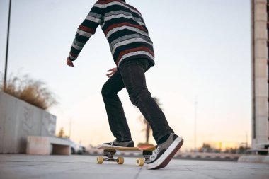 Beyaz tenli, çizgili spor ayakkabılı bir adam açık bir günde gün batımında şehirde kaykaya biniyor.