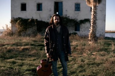 Beyaz gitarist çocuk terk edilmiş evin yanında elinde İspanyol gitarıyla duruyor. Maço yaşam tarzı.