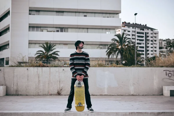 Καυκάσιος Νεαρός Άνδρας Ριγέ Πουλόβερ Στέκεται Ανοιχτά Πόδια Κρατώντας Skateboard — Φωτογραφία Αρχείου