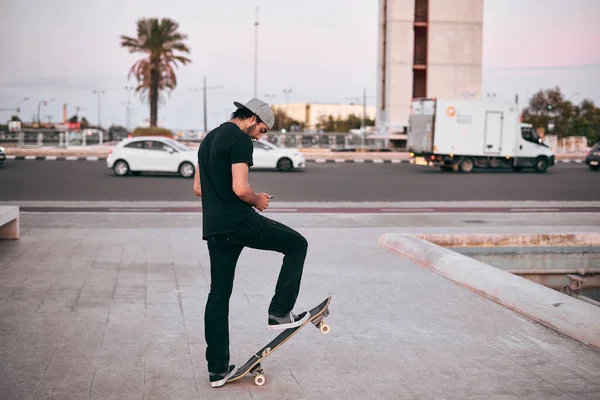 Kaukasische Jongeman Zwart Shirt Pet Zijn Hoofd Staand Zijn Skateboard — Stockfoto