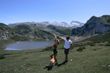 Kafkasyalı genç kadın ve Latin erkek sakin ve rahat bir şekilde dans ediyor göl kenarında köpeğiyle dans ediyor, covadonga asturias, spain - ulusal park